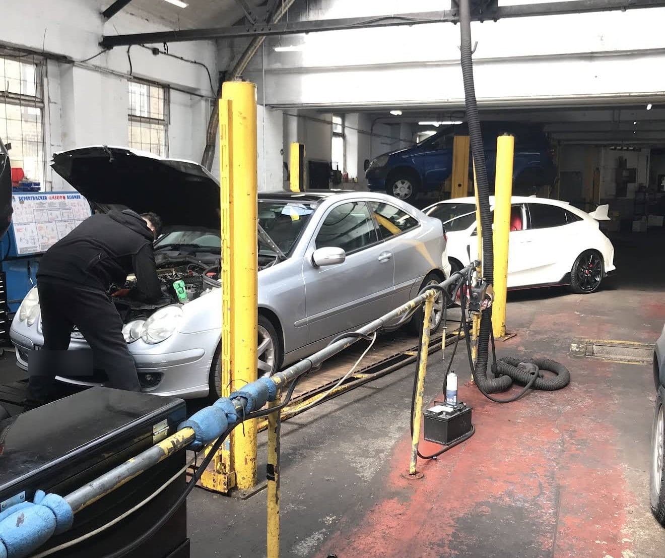 A Surefix mechanic working under the bonnet of a silver Mercedes in the Halifax workshop
